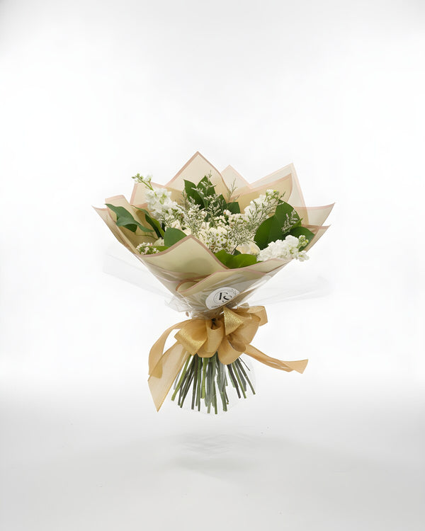 Paper White — a bouquet of all-white blooms, roses, stock, and seasonal accents, wrapped in natural kraft paper for an understated, elegant look