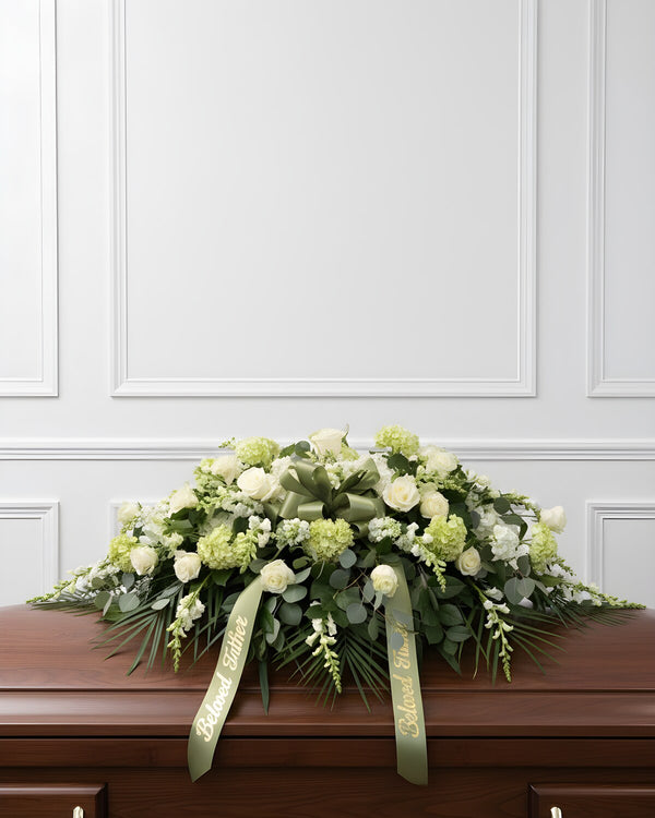 Quiet White Casket Spray — a serene casket spray of white roses, snapdragons, mums, and hydrangea, accented with soft greenery