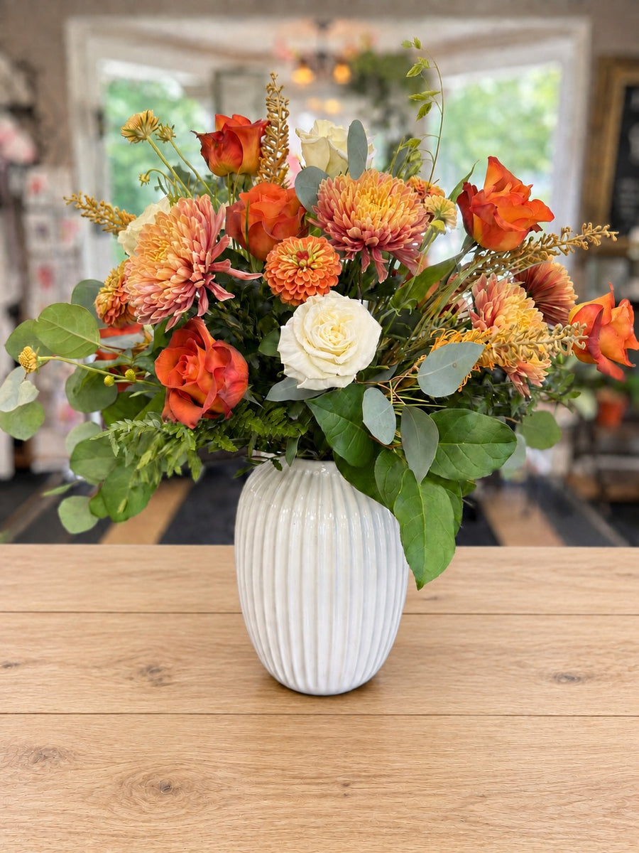 Fall arrangement of orange roses, peach mums, zinnias and white roses in a ribbed white vase at Four Seasons Flower Shop